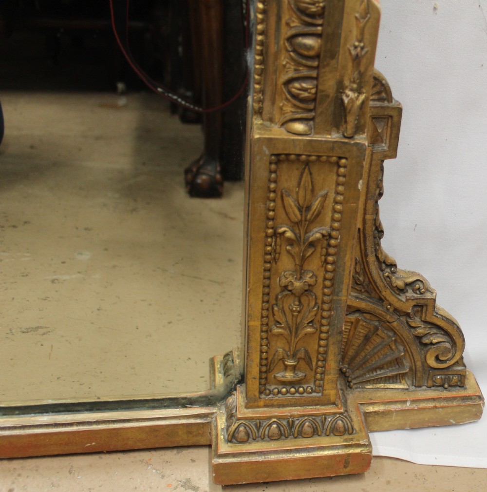 A large rectangular gilded overmantel mirror featuring a moulded frame with floral swags, a guilloche frieze, and decorative plinth bases. View IV