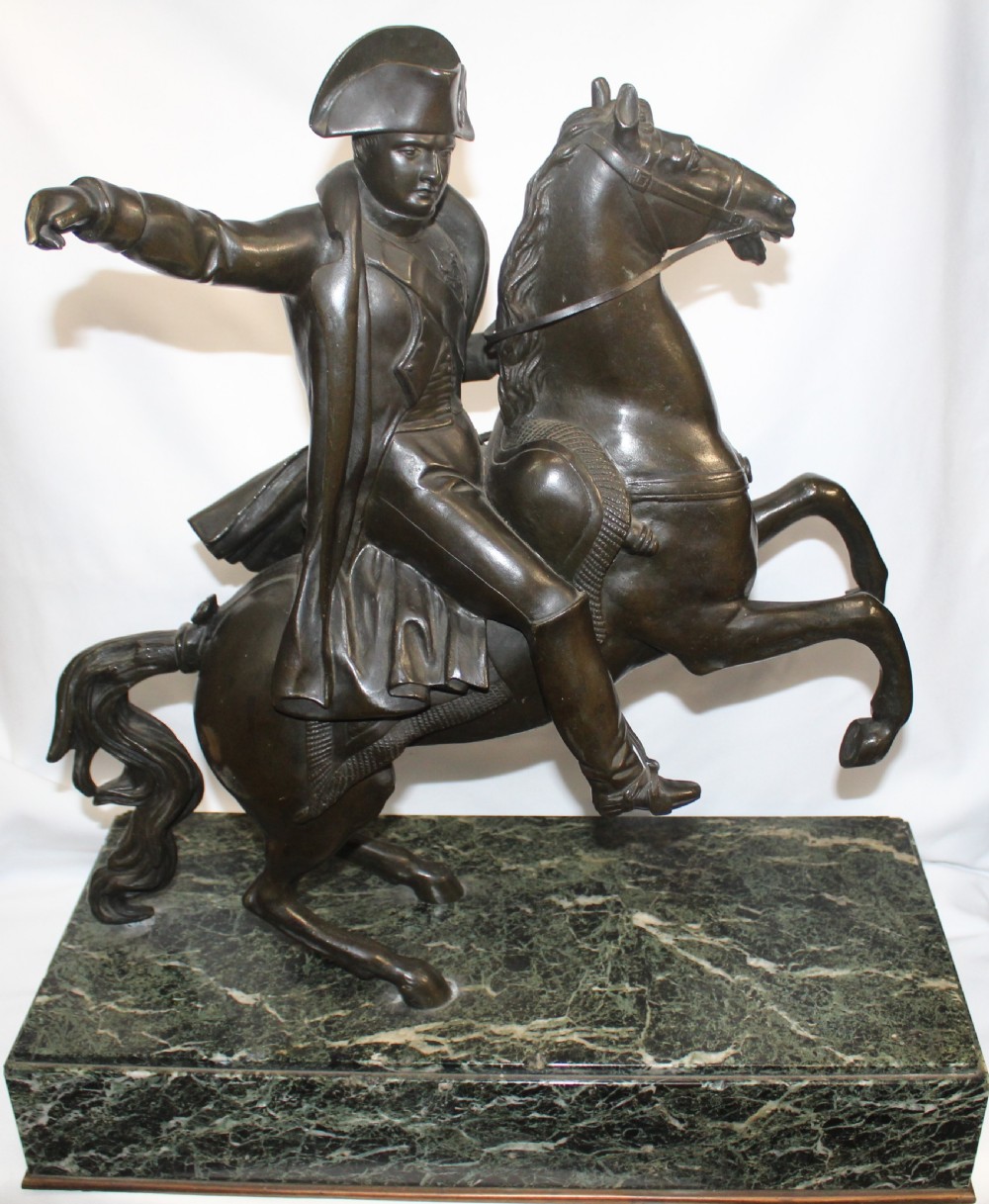 A patinated bronze sculpture depicting Napoleon Bonaparte riding a rearing horse, mounted on a polished green marble rectangular base.