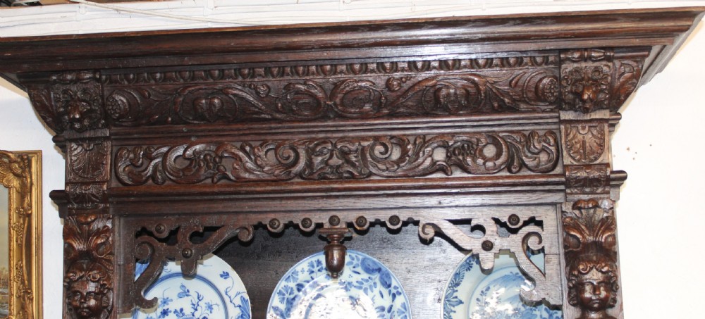 A dark carved oak wall-mounted plate rack featuring three shelves, flanked by carved caryatid figures and topped with a moulded ornate cornice. View II