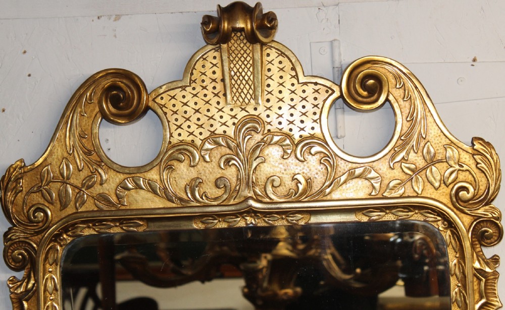 An antique gilded wall mirror featuring scrolled cresting, carved floral leaf motifs, and a rectangular glass plate. View II