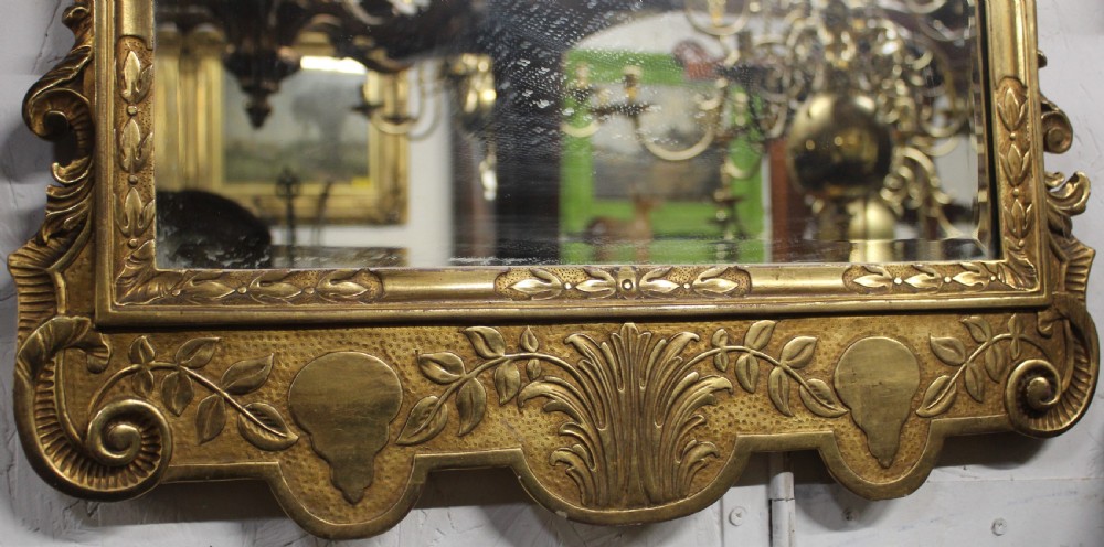 An antique gilded wall mirror featuring scrolled cresting, carved floral leaf motifs, and a rectangular glass plate. View III