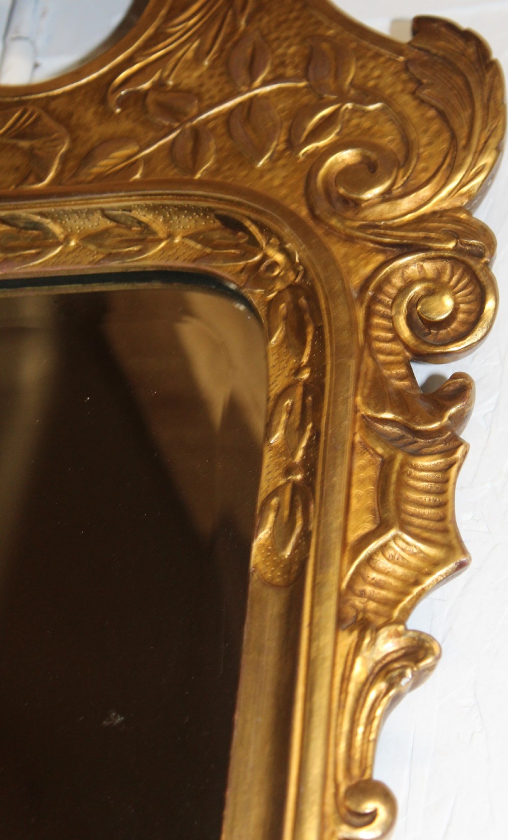 An antique gilded wall mirror featuring scrolled cresting, carved floral leaf motifs, and a rectangular glass plate. View V