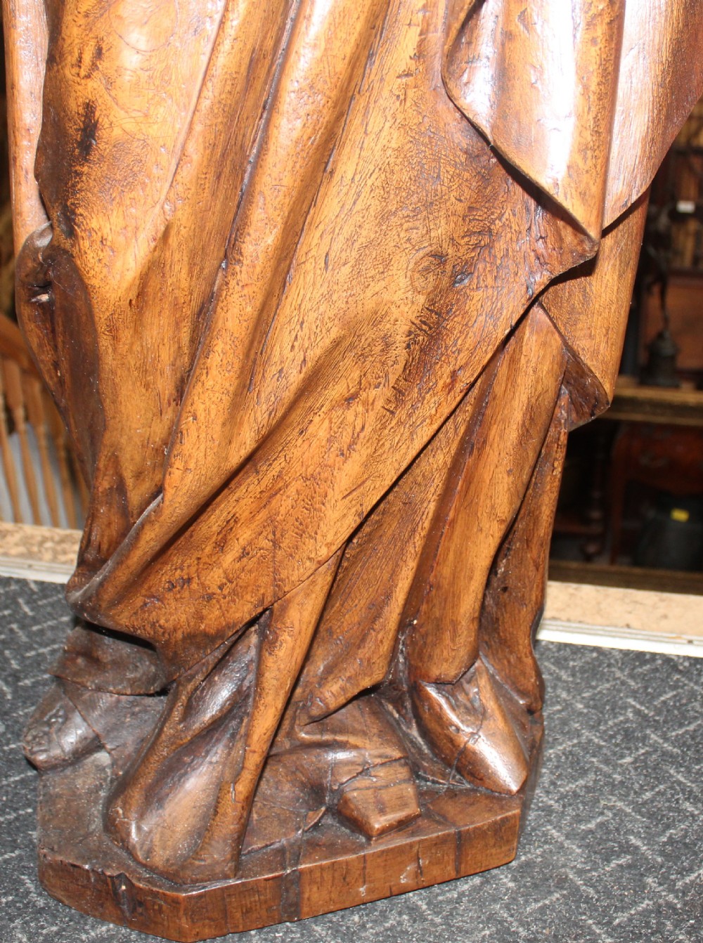 A dark hand-carved wooden statue depicting the Virgin Mary standing and holding the infant Christ in draped robes. View V