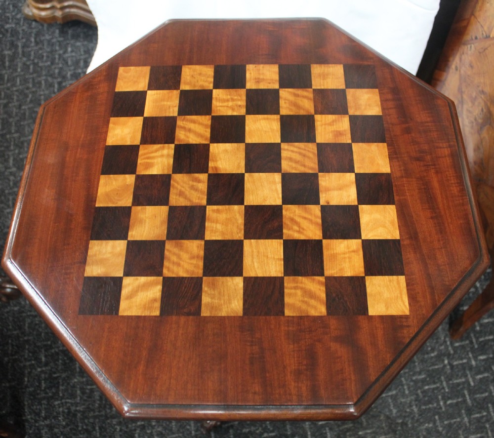 An octagonal mahogany games table featuring an inlaid chessboard top on a central turned pedestal with carved tripod legs. View V