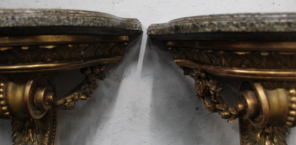 A pair of wall-mounted giltwood console tables with single carved scroll bracket legs and shaped marble tops. View IV