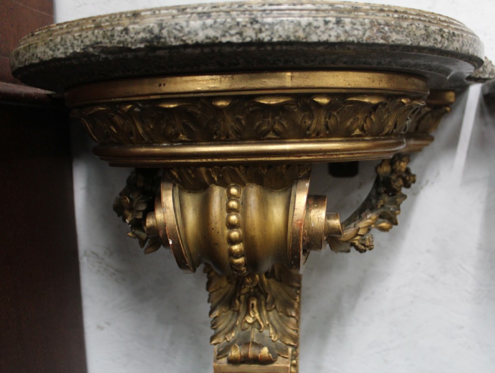 A pair of wall-mounted giltwood console tables with single carved scroll bracket legs and shaped marble tops. View V