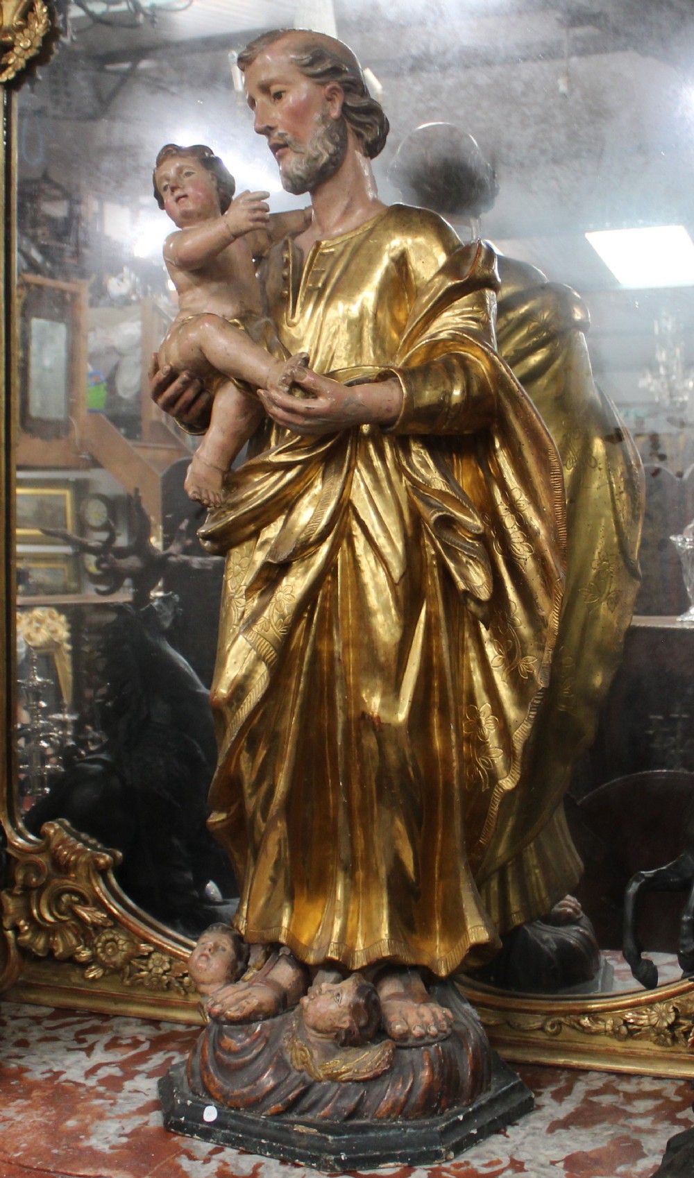 A carved wooden statue depicting Saint Joseph holding the infant Jesus, finished with gold leaf gilding and painted features atop a cherub base.