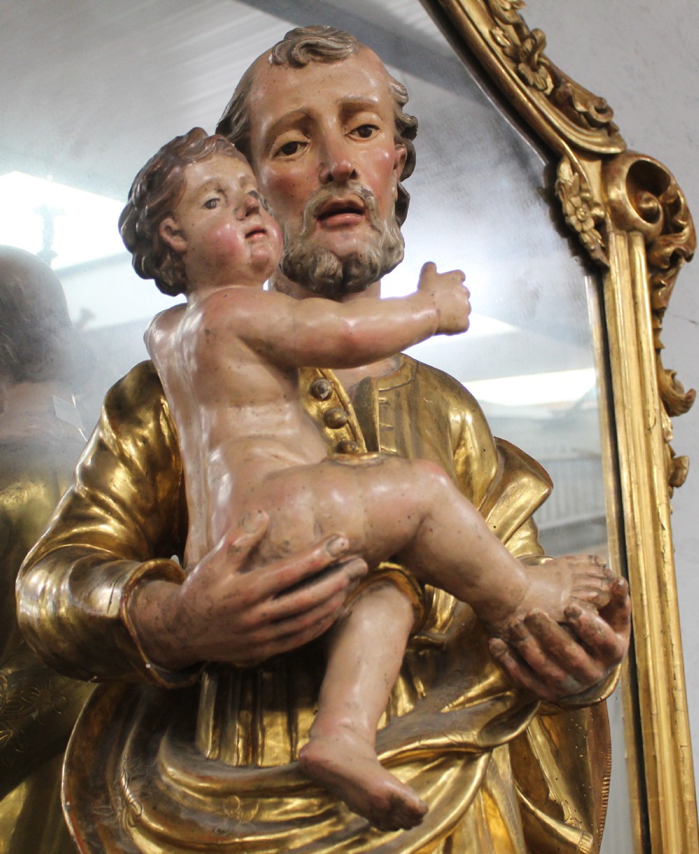 A carved wooden statue depicting Saint Joseph holding the infant Jesus, finished with gold leaf gilding and painted features atop a cherub base. View II