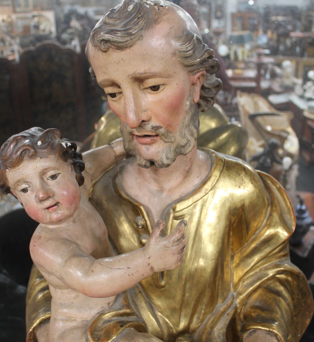 A carved wooden statue depicting Saint Joseph holding the infant Jesus, finished with gold leaf gilding and painted features atop a cherub base. View XIII