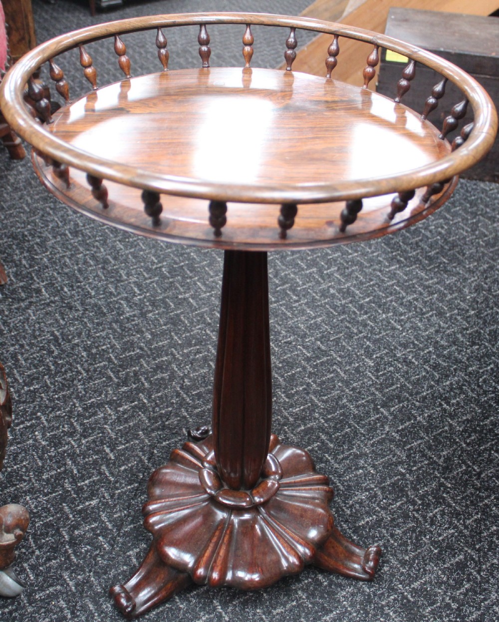 A dark rosewood circular wine table featuring a spindled gallery rim, a turned column stem, and a carved lobed base.