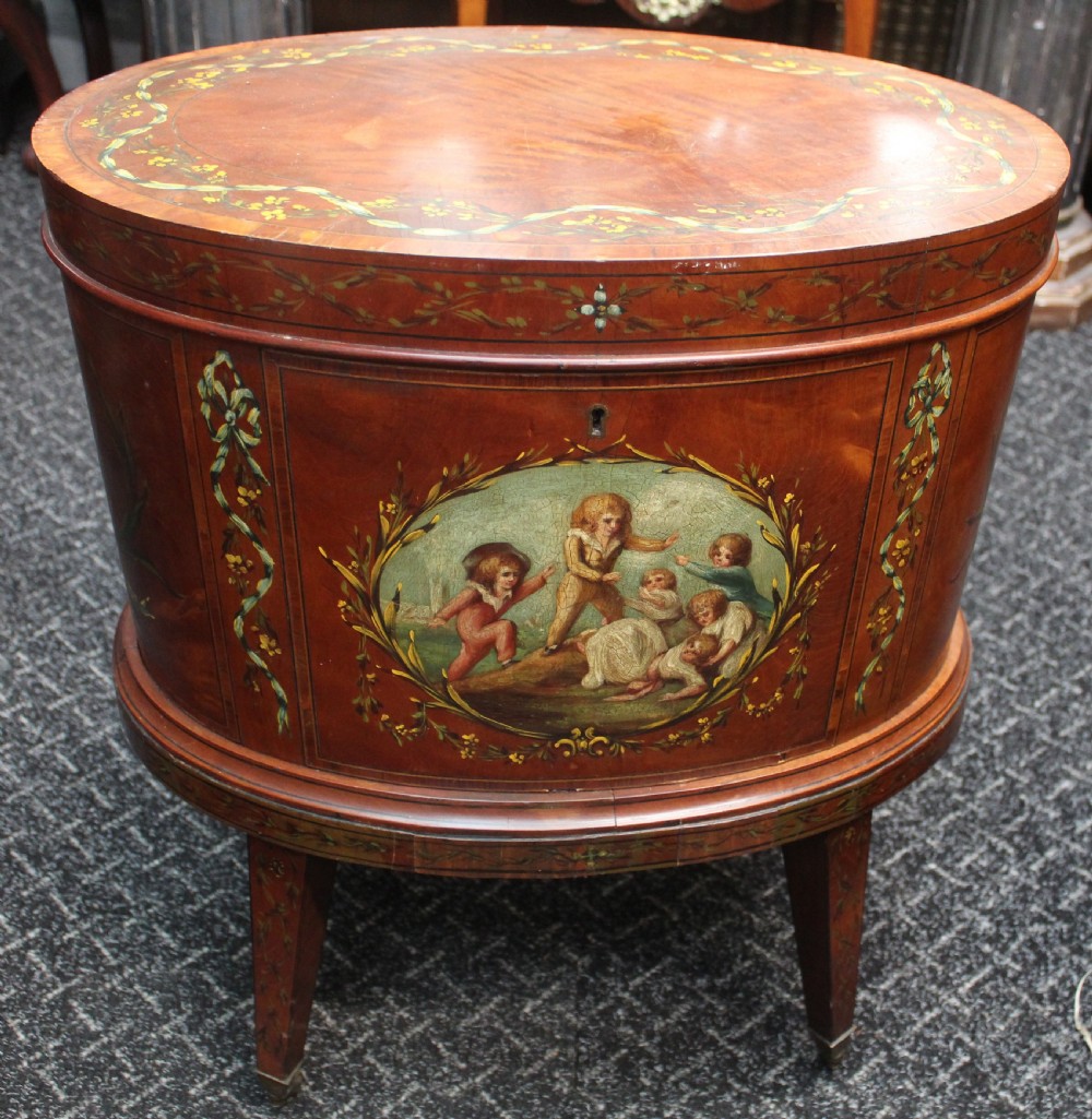 An oval antique satinwood wine cooler featuring hand-painted figurative scenes and floral garlands supported by tapered legs.