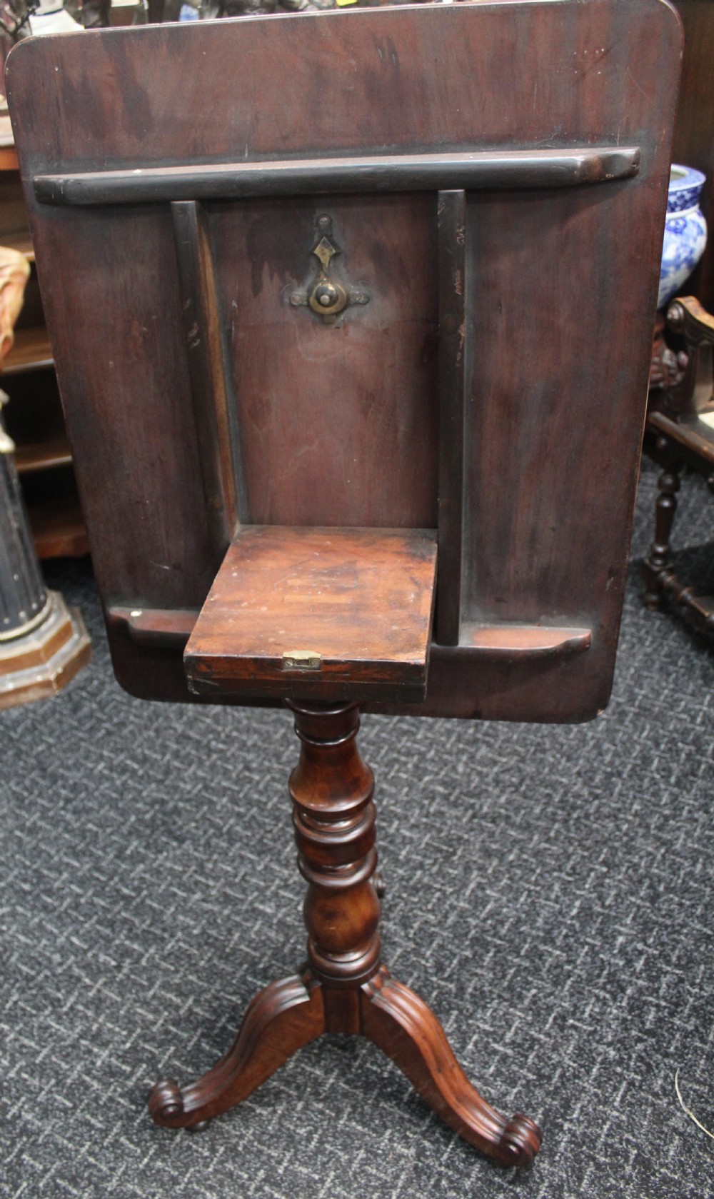 An antique mahogany tilt-top wine table shown with its top tilted upright on a turned pedestal stem and tripod scrolled legs. View III