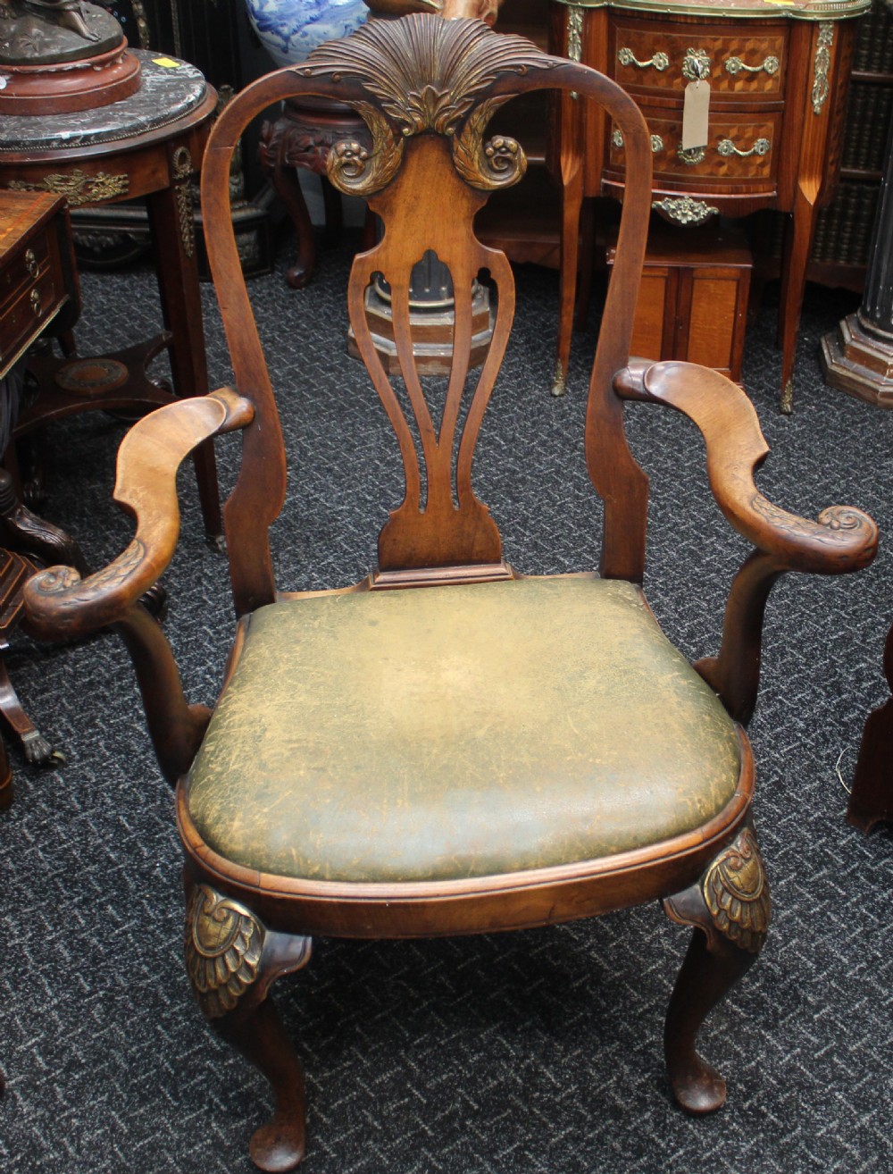 An antique Chippendale style carved mahogany open armchair with a shell crest, pierced splat back, carved cabriole legs, and an aged green leather drop-in seat pad.