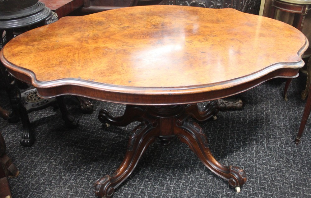 A Victorian burr walnut tilt-top loo table featuring a book-matched serpentine top set on a carved pedestal base with four scrolled legs. View II