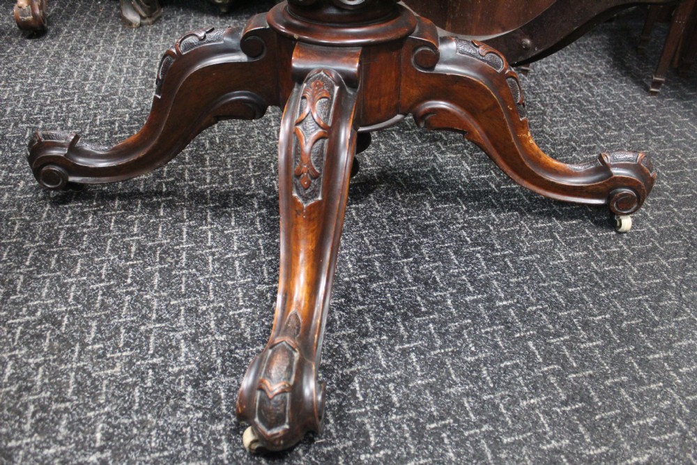 A Victorian burr walnut tilt-top loo table featuring a book-matched serpentine top set on a carved pedestal base with four scrolled legs. View V