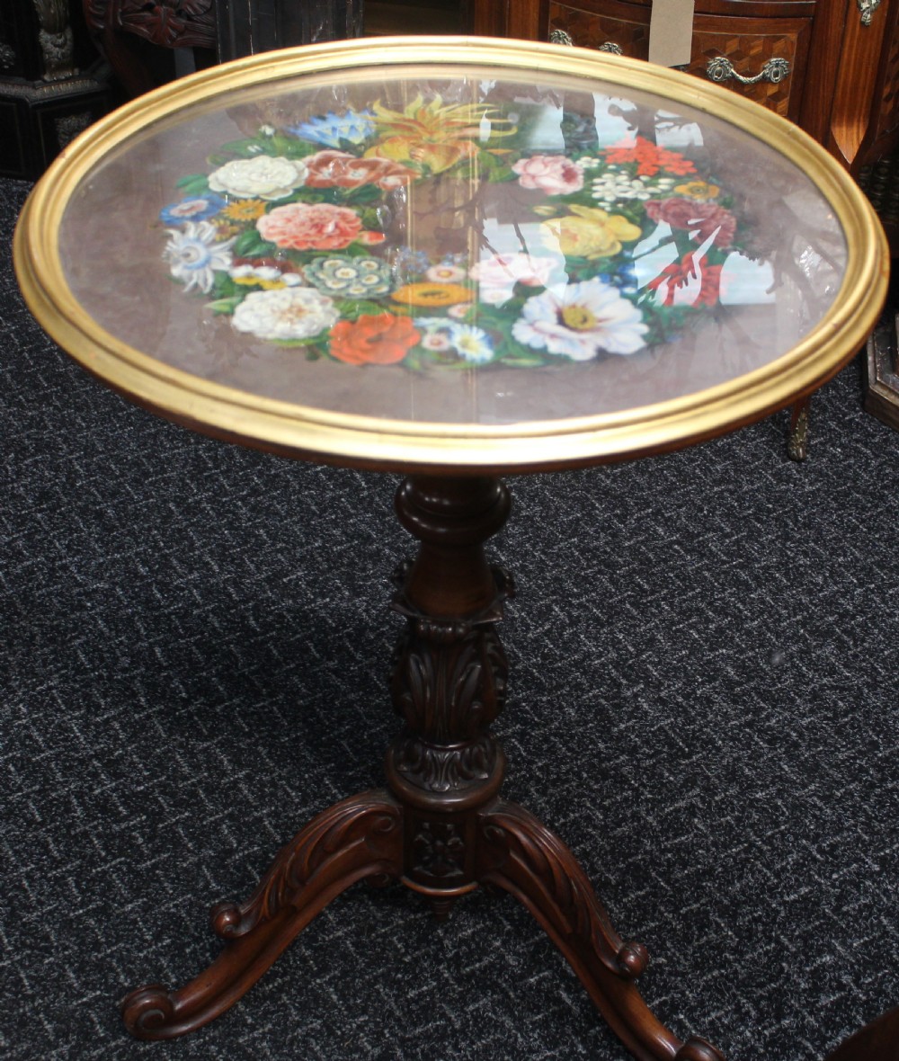 A Victorian circular occasional table featuring a hand-painted floral wreath top enclosed in a gold moulding, supported by a carved wooden pedestal and tripod scroll legs. View II