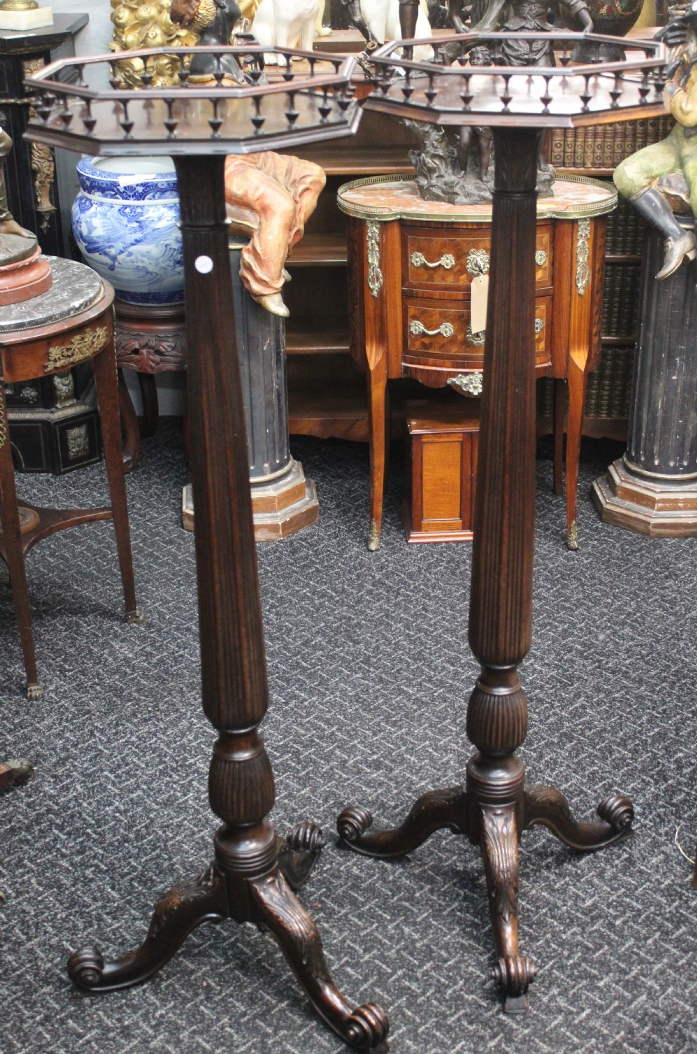 A pair of tall dark mahogany torchere stands featuring octagonal gallery tops, fluted stems, and carved tripod scroll legs.