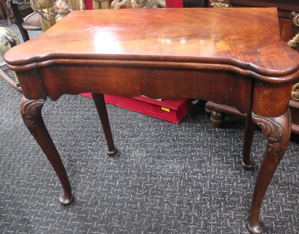 An antique mahogany fold-over games table featuring carved cabriole legs with pad feet and a shaped serpentine top.