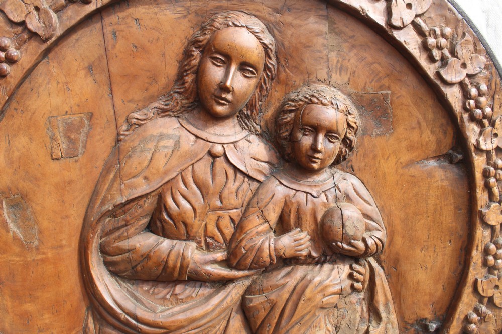A circular hand-carved wooden relief plaque depicting the Madonna and Child surrounded by a carved floral border. View II