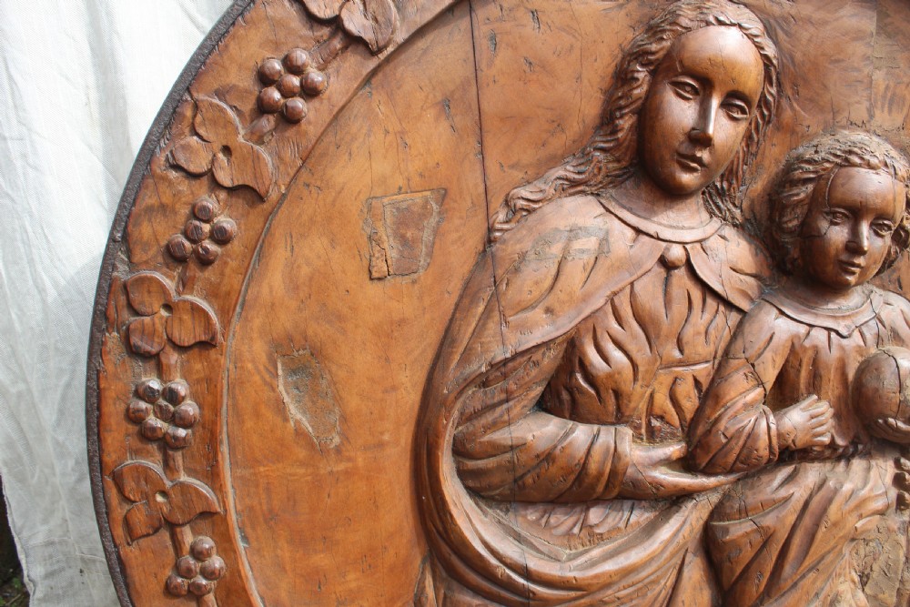 A circular hand-carved wooden relief plaque depicting the Madonna and Child surrounded by a carved floral border. View III
