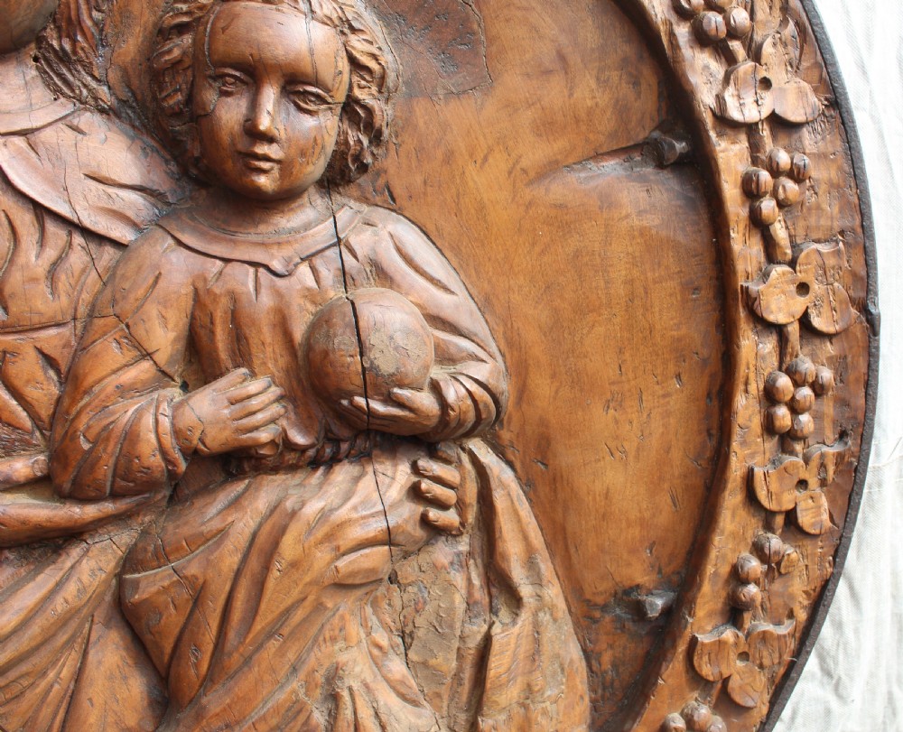 A circular hand-carved wooden relief plaque depicting the Madonna and Child surrounded by a carved floral border. View IV