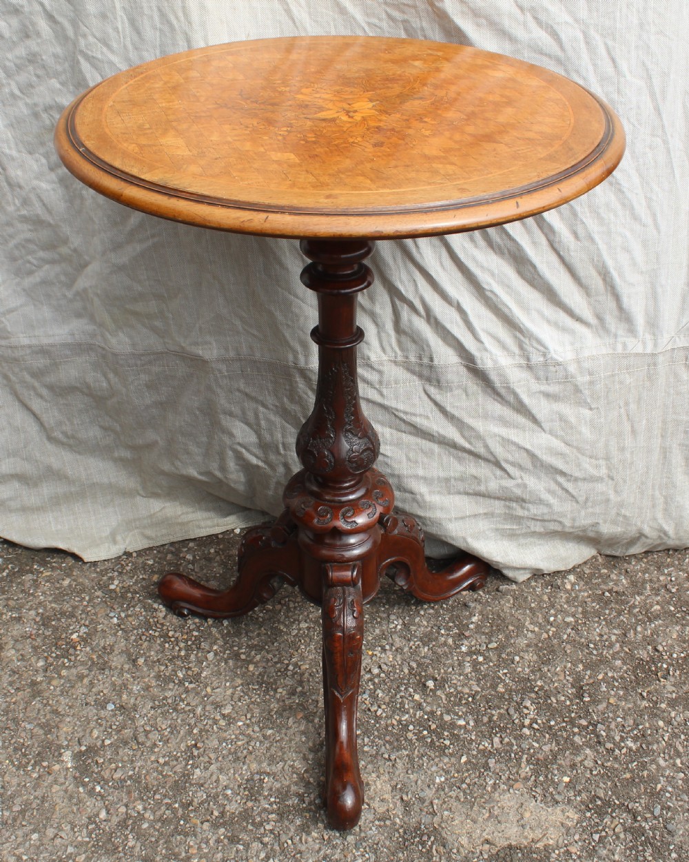 A circular antique wine table with a light parquetry inlaid top featuring a floral central motif on a carved dark mahogany tripod pedestal.