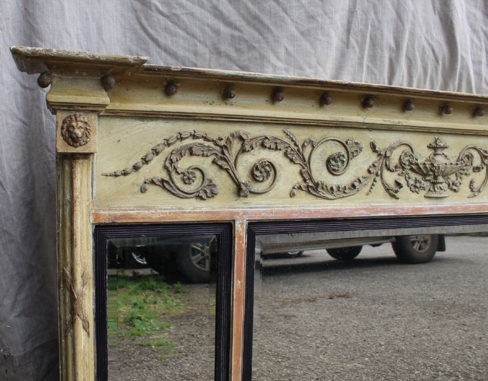 A wide horizontal antique overmantel mirror featuring a distressed cream painted finish, carved neoclassical urn motifs, and three distinct mirror panels. View II