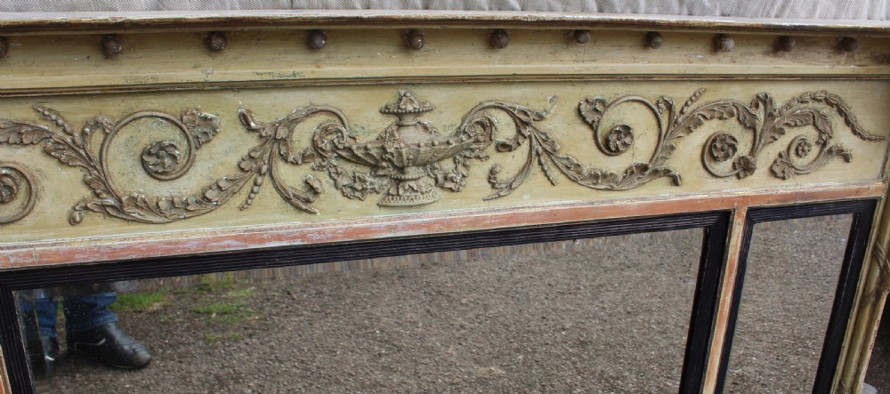 A wide horizontal antique overmantel mirror featuring a distressed cream painted finish, carved neoclassical urn motifs, and three distinct mirror panels. View IV
