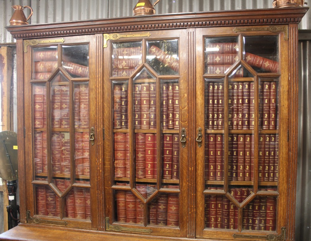 A large English oak glazed bookcase featuring three upper glass doors with geometric mullions above three drawers and three geometric panelled cupboard doors with brass mounts. View II