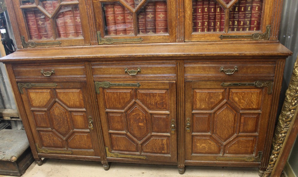 A large English oak glazed bookcase featuring three upper glass doors with geometric mullions above three drawers and three geometric panelled cupboard doors with brass mounts. View III