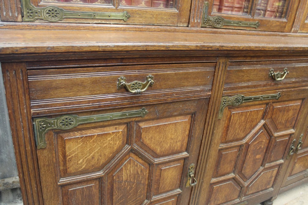 A large English oak glazed bookcase featuring three upper glass doors with geometric mullions above three drawers and three geometric panelled cupboard doors with brass mounts. View V