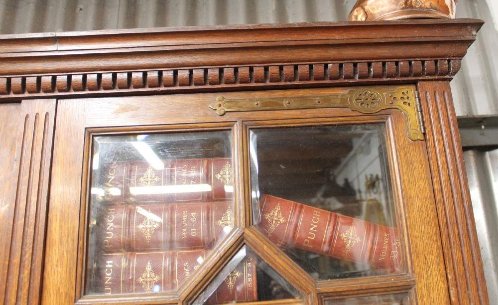 A large English oak glazed bookcase featuring three upper glass doors with geometric mullions above three drawers and three geometric panelled cupboard doors with brass mounts. View VI