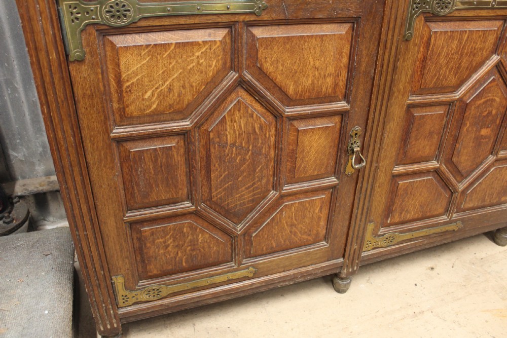 A large English oak glazed bookcase featuring three upper glass doors with geometric mullions above three drawers and three geometric panelled cupboard doors with brass mounts. View VII
