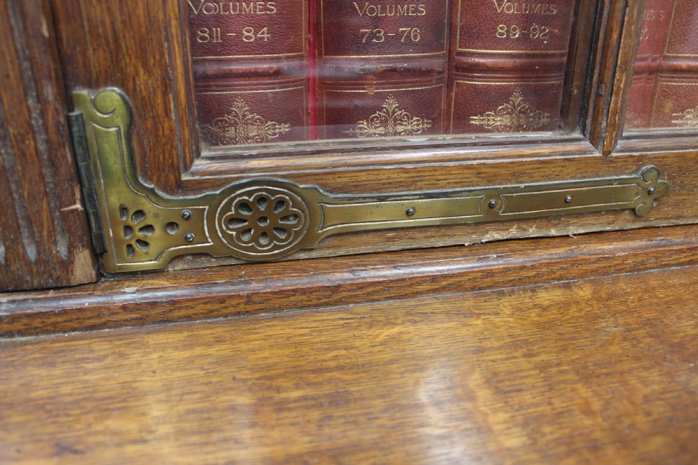 A large English oak glazed bookcase featuring three upper glass doors with geometric mullions above three drawers and three geometric panelled cupboard doors with brass mounts. View VIII