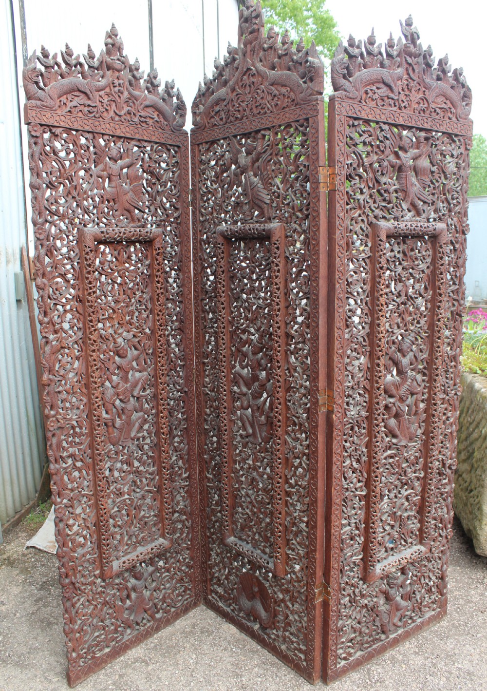 A three-panel dark wood folding screen featuring intricate hand-carved openwork lattice, floral scrolls, mythological figures, and a decorative crest.