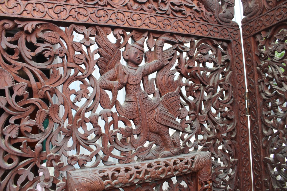 A three-panel dark wood folding screen featuring intricate hand-carved openwork lattice, floral scrolls, mythological figures, and a decorative crest. View III