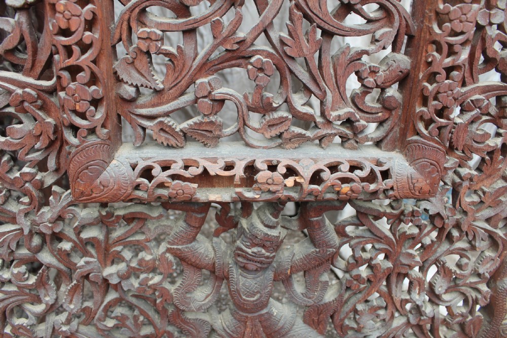 A three-panel dark wood folding screen featuring intricate hand-carved openwork lattice, floral scrolls, mythological figures, and a decorative crest. View V