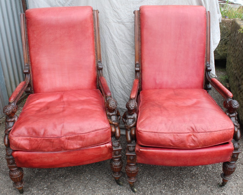 A pair of French armchairs upholstered in red leather with dark carved wood frames featuring cherub figures on the arm supports.