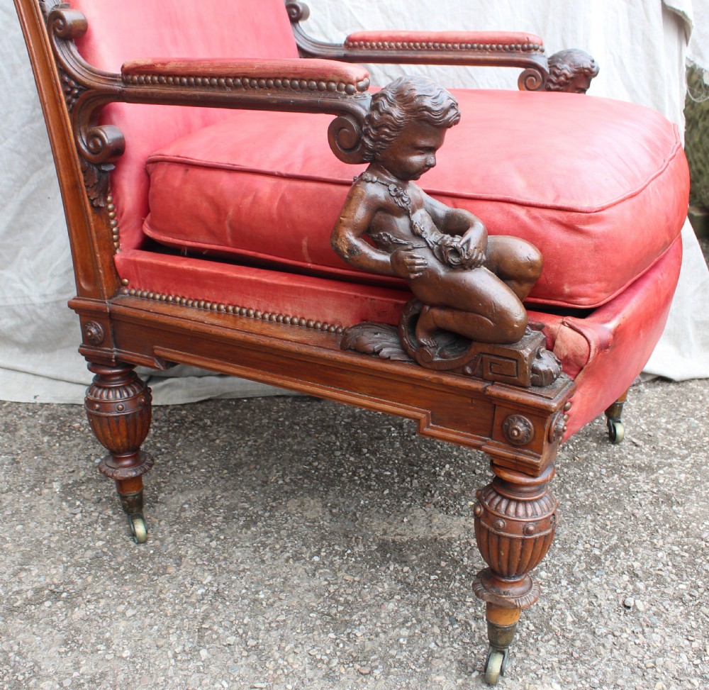 A pair of French armchairs upholstered in red leather with dark carved wood frames featuring cherub figures on the arm supports. View II