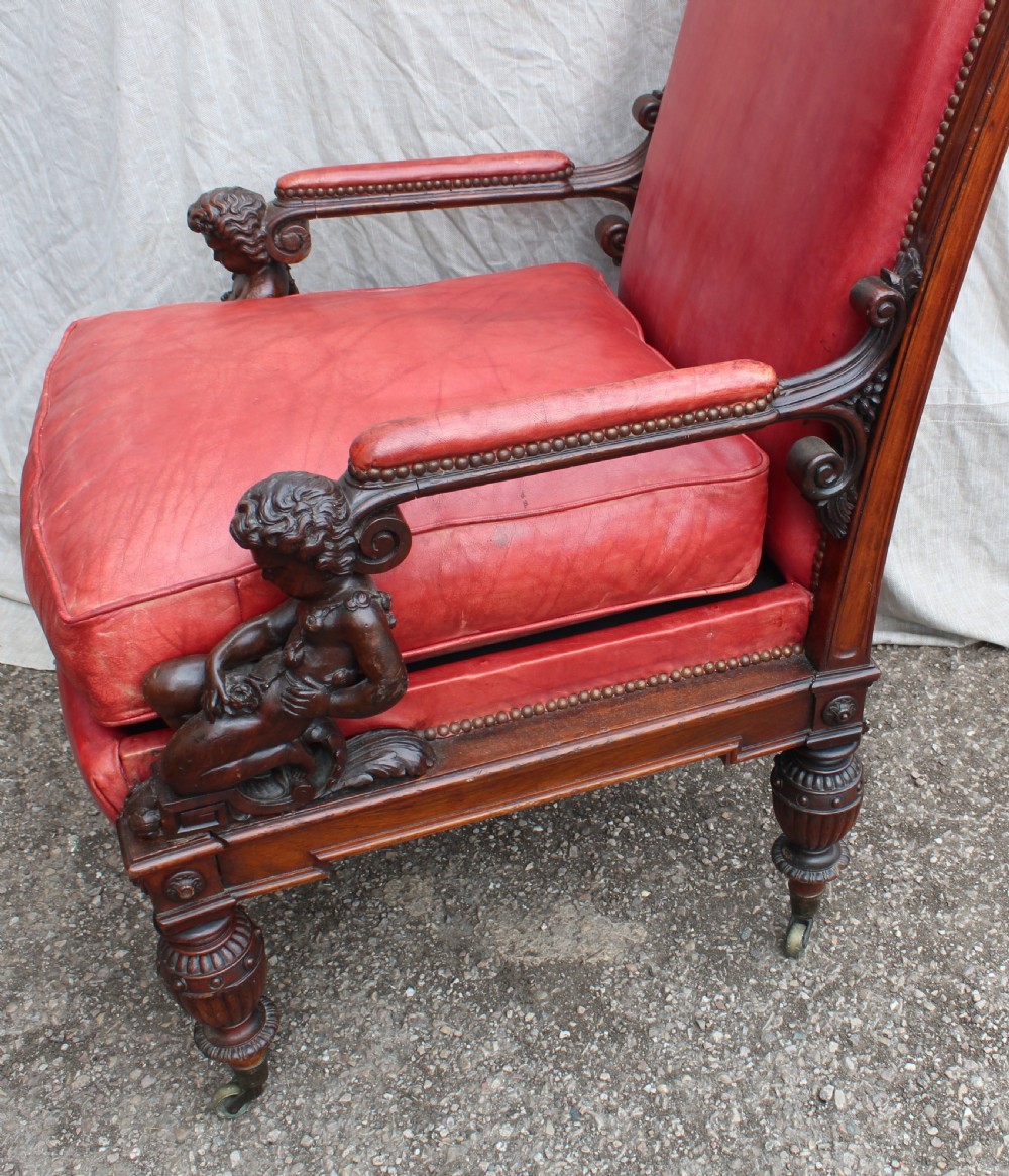 A pair of French armchairs upholstered in red leather with dark carved wood frames featuring cherub figures on the arm supports. View V