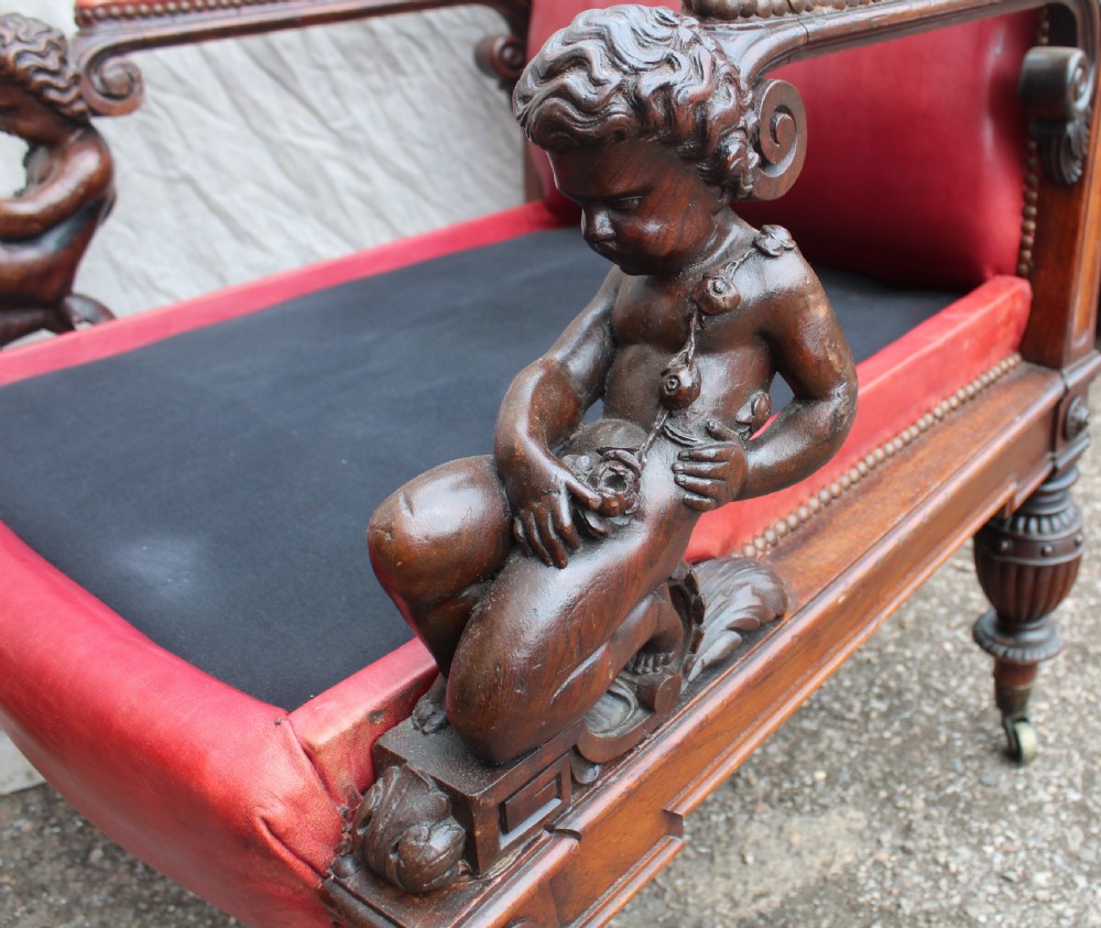 A pair of French armchairs upholstered in red leather with dark carved wood frames featuring cherub figures on the arm supports. View VI