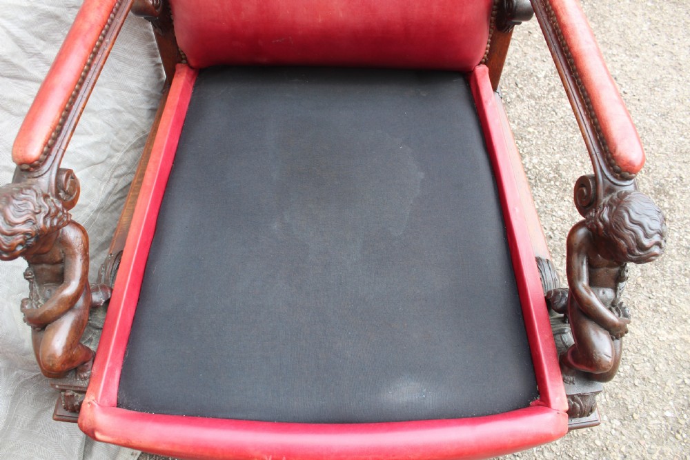 A pair of French armchairs upholstered in red leather with dark carved wood frames featuring cherub figures on the arm supports. View VII