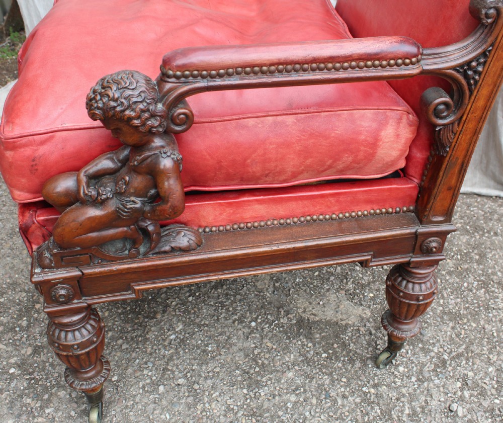 A pair of French armchairs upholstered in red leather with dark carved wood frames featuring cherub figures on the arm supports. View VIII
