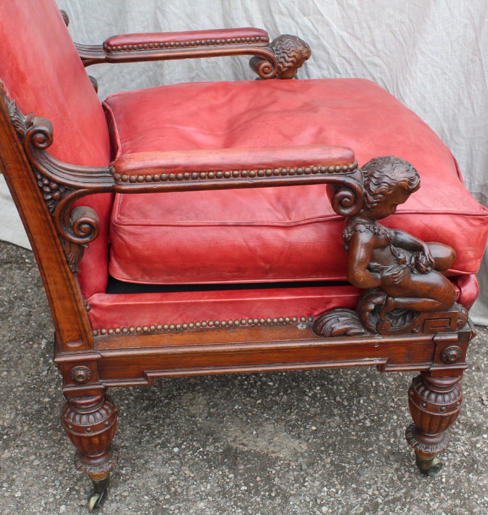 A pair of French armchairs upholstered in red leather with dark carved wood frames featuring cherub figures on the arm supports. View X