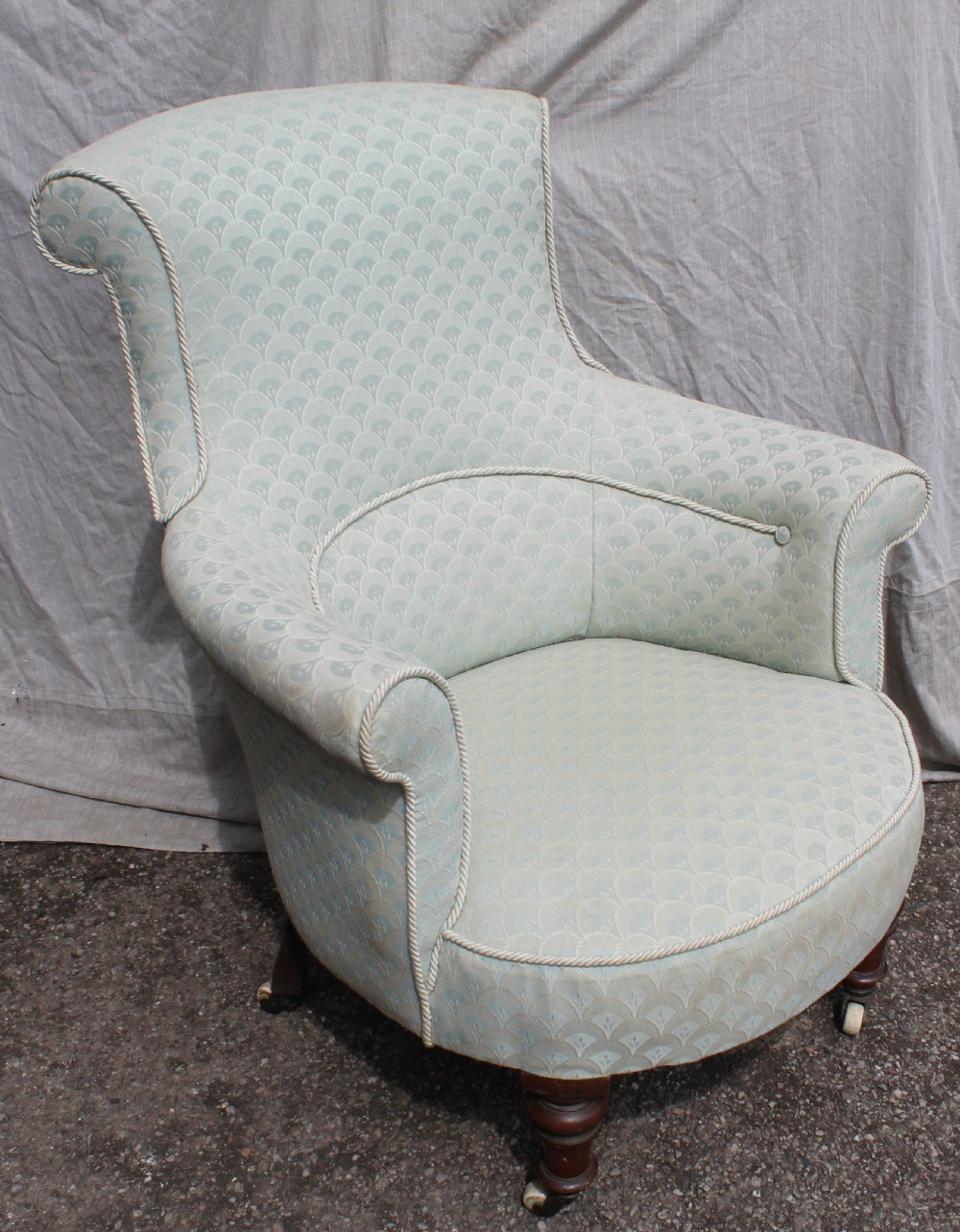 Victorian low upholstered armchair featuring pale duck egg blue patterned fabric with light rope piping and turned dark mahogany legs on ceramic castors.