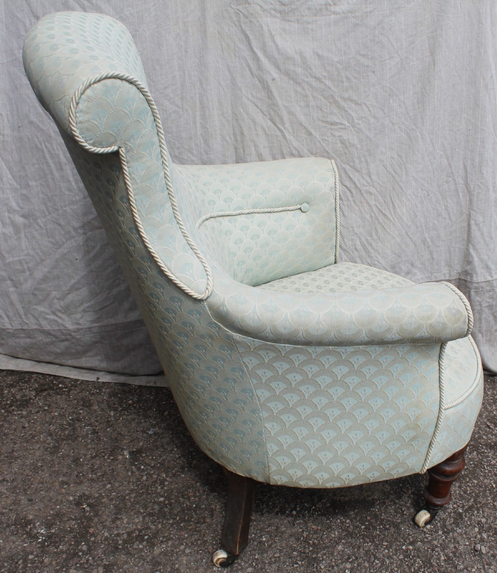 Victorian low upholstered armchair featuring pale duck egg blue patterned fabric with light rope piping and turned dark mahogany legs on ceramic castors. View II