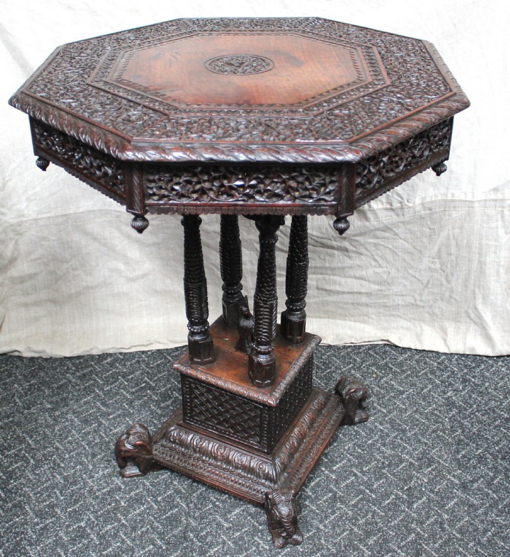A dark brown hand-carved octagonal wooden occasional table featuring turned pillars and carved elephant head feet.
