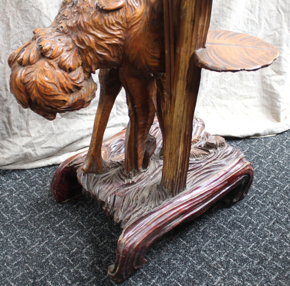An intricately carved brown wooden pedestal stand featuring putti riding an ostrich surrounded by foliage, topped with a lily pad shaped platform. View VIII