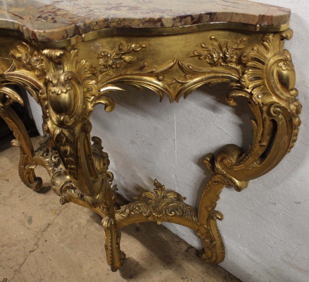 A Rococo style giltwood console table featuring ornate acanthus leaf carving, C-scroll legs, a central shell motif stretcher, and a serpentine variegated marble top. View II