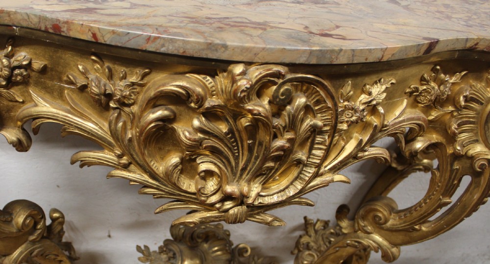 A Rococo style giltwood console table featuring ornate acanthus leaf carving, C-scroll legs, a central shell motif stretcher, and a serpentine variegated marble top. View III